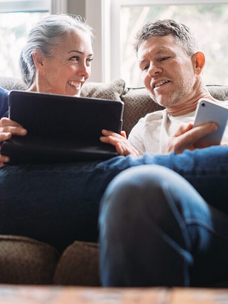 Man and woman are sitting down holding a tablet and phone.