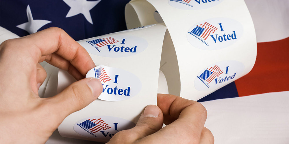 Hands removing "I Voted" sticker from roll of stickers.