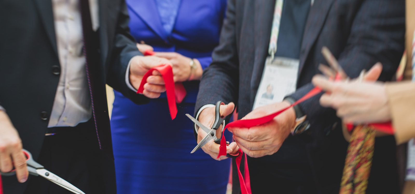 Process of cutting the red ribbon during the grand opening of the new shopping center mall building, opening of exhibition, close up view of red ribbon with people around